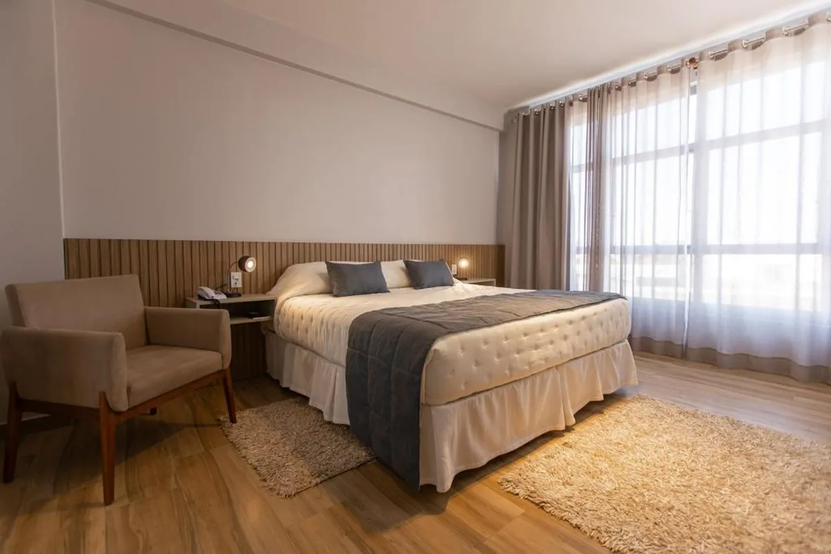 Quarto do BM Hotel com cama de casal e poltrona junto à janela